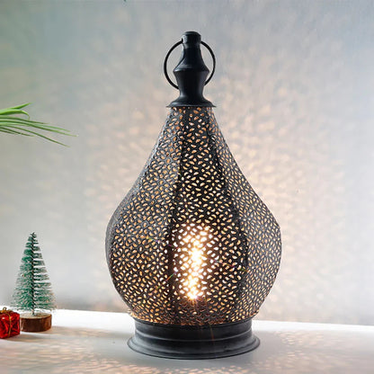 Een elegante tafel lamp met een uniek geperforeerd ontwerp in de vorm van een waterdruppel. Het zachte licht straalt door de openingen in het metaal, waardoor mooie schaduwen op de muur ontstaan. De lamp staat op een tafel, omringd door feestelijke kerstdecoraties zoals een klein kerstboompje en een cadeau. Perfect om een sfeervolle en verfijnde uitstraling aan je interieur toe te voegen.